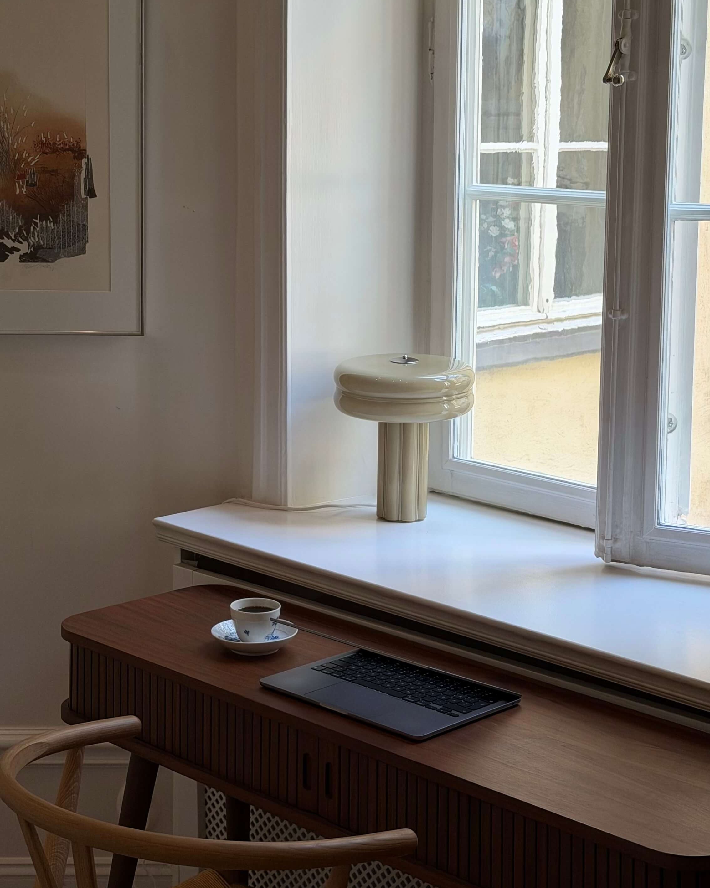 Table lamp in Sage green standing in a window in front of  work desk setup. 