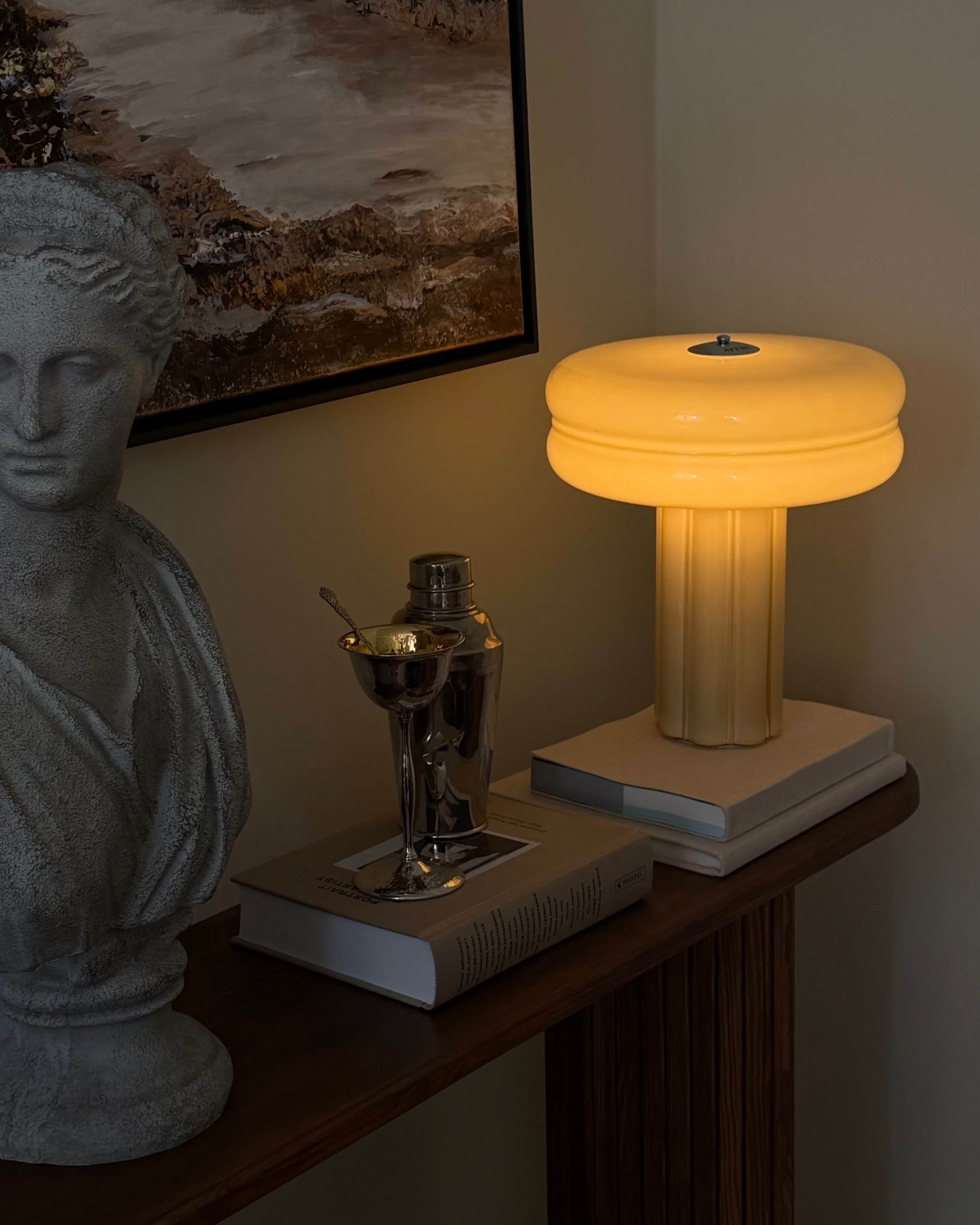 Affiné table lamp with soft amber glow and dimmer, styled on a bookstack on a side table