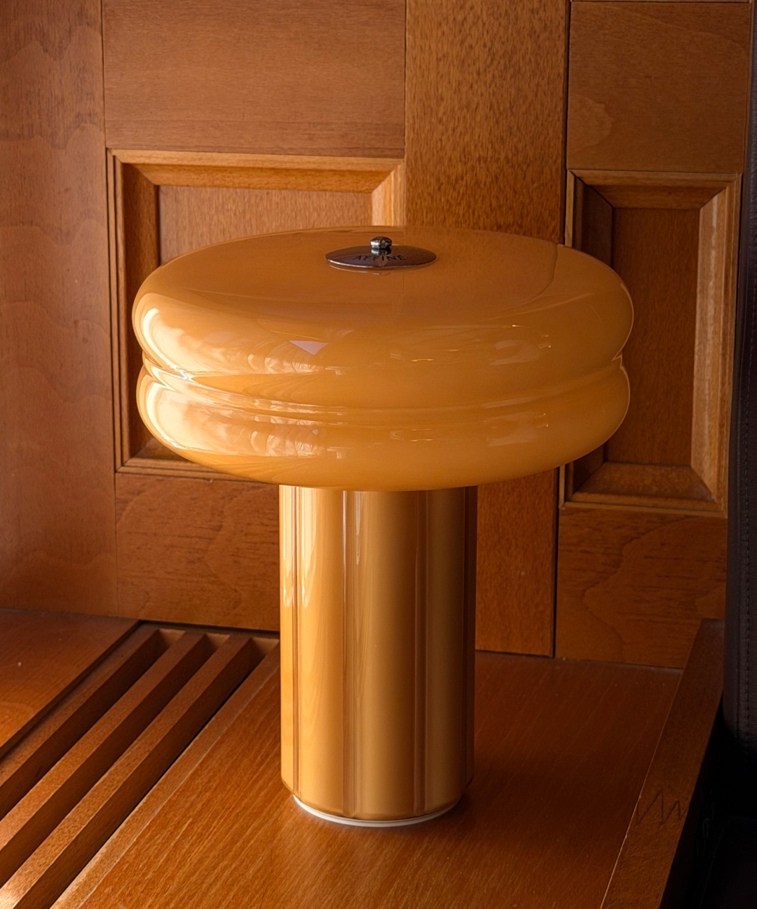 Affiné Portable Lamp in Soft Amber placed by a wooden-framed window.