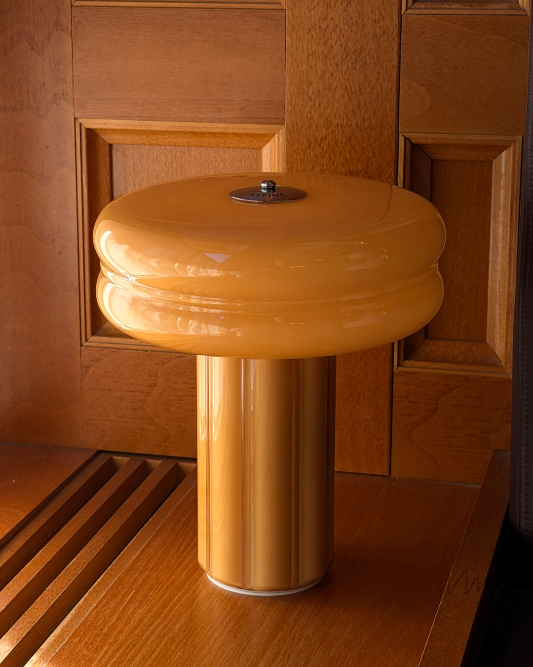 Affiné Portable Lamp in Soft Amber placed by a wooden-framed window.