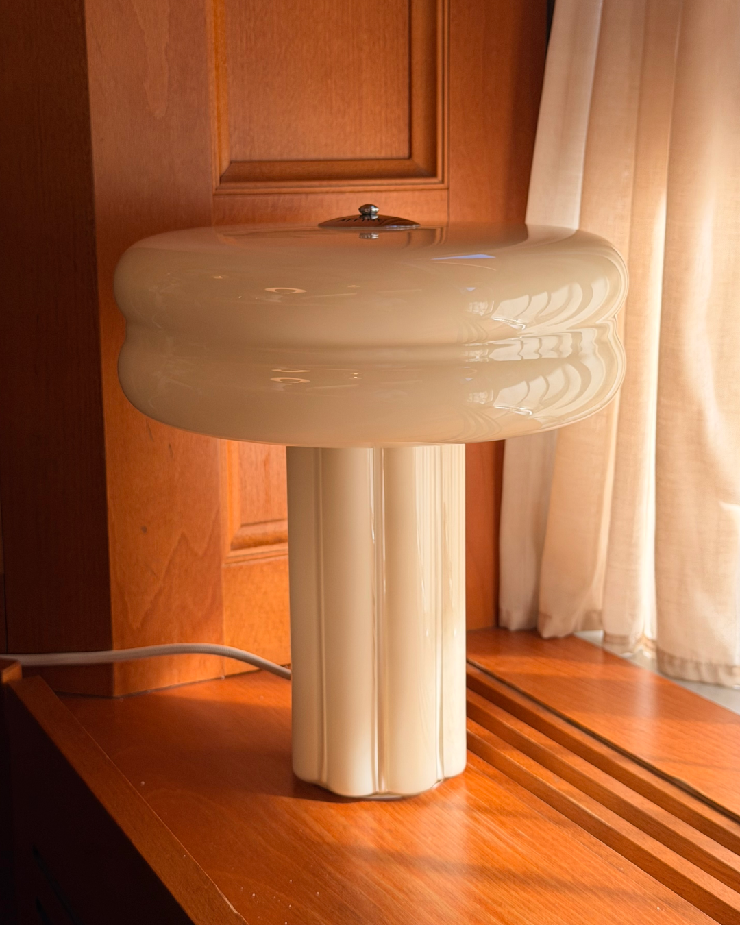 The Affiné Table Lamp in Crème Beige in a wooden-framed window.