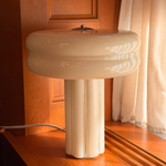 The Affiné Table Lamp in Crème Beige in a wooden-framed window.