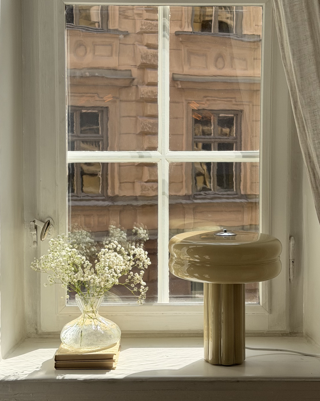 The Affiné Table Lamp in Sage Green glowing by a window.