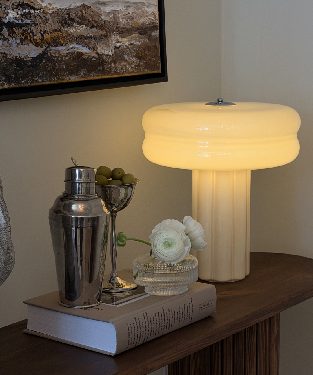 Affiné Table Lamp in Crème Beige styled on a dark wooden sideboard.